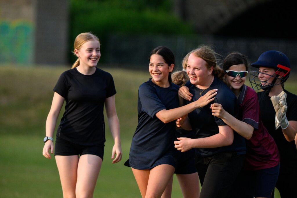 Group of teenage girls wearing sports clothes cheering and celebrating after scoring during a friendly cricket match